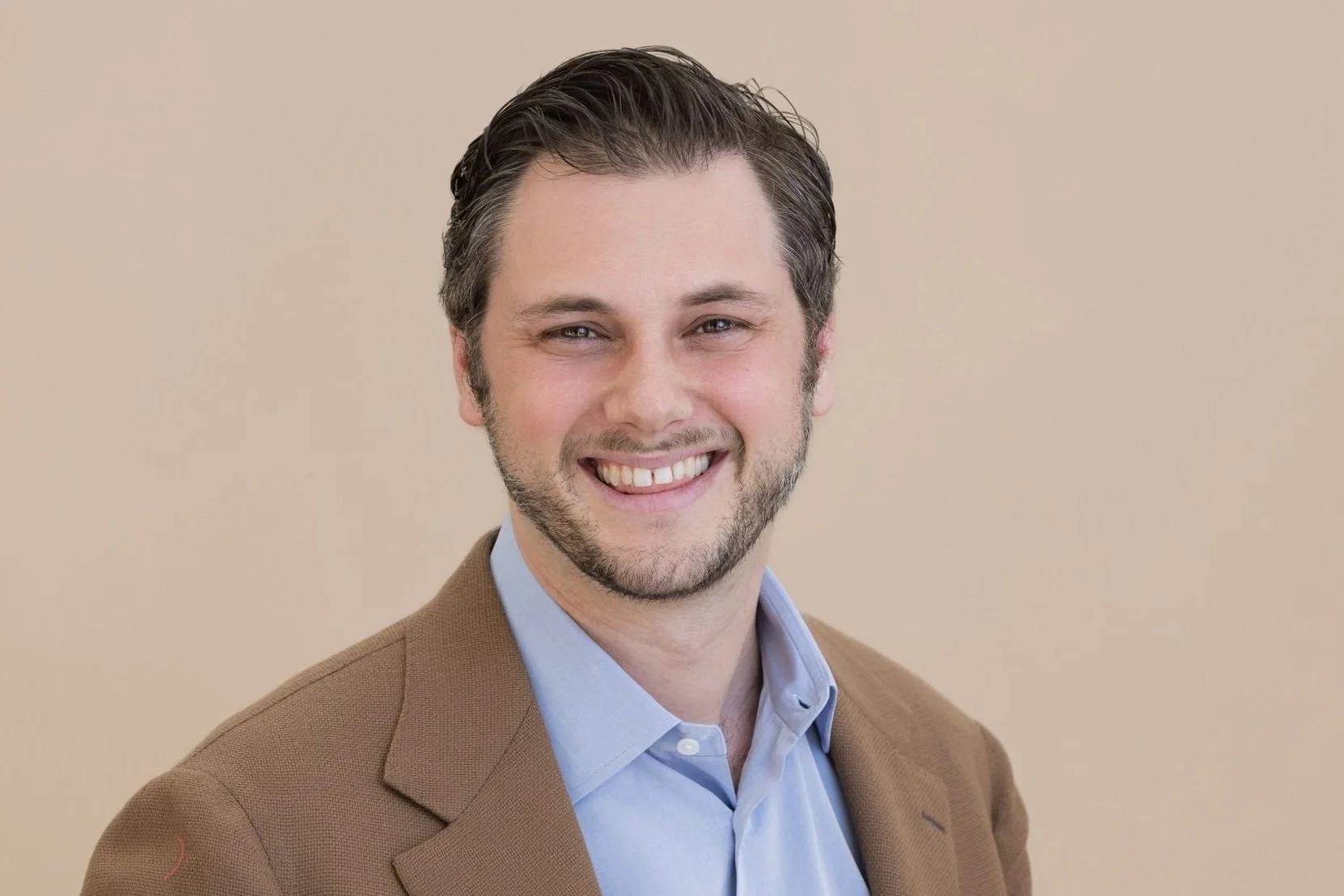 Adam Rosenwach smiling with a beige background